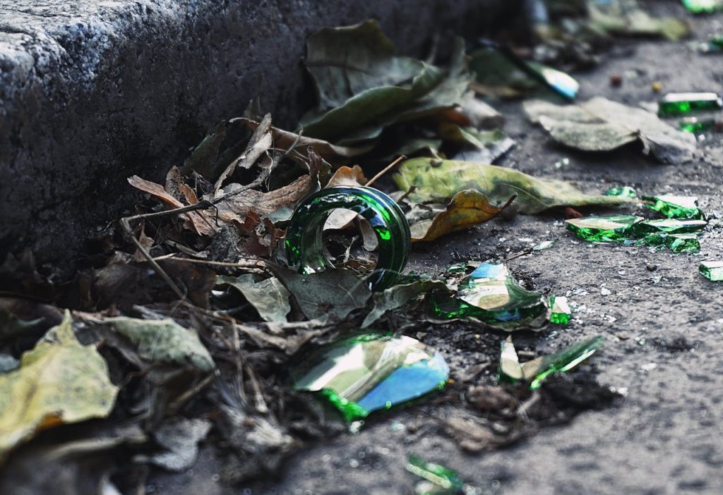 Close-up of shattered green glass amidst fallen leaves, highlighting urban waste.