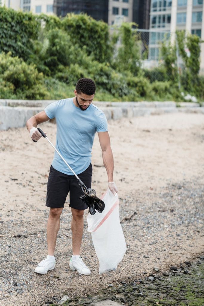 Young man picking up plastic waste on a beach, promoting environmental conservation.