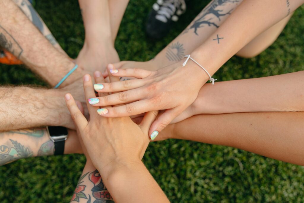 A group of people's hands with tattoos and colorful nails symbolizing unity on grass.